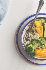 Vegan buddha bowl with brown rice, broccoli and vegetables in a white plate on a white background, copy space, top view.