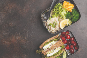 Healthy meal prep containers with feta sandwich with fruits, berries, rice and vegetables on dark background, top view. © vaaseenaa