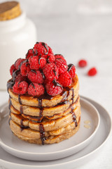 Homemade pancakes with raspberries and chocolate on a white plate, white background. Healthy vegan food concept.