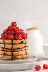 Homemade pancakes with raspberries and chocolate on a white plate, white background. Healthy vegan food concept.
