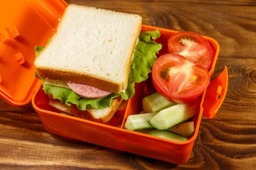 School lunch box with sandwich and fresh vegetables on wooden table