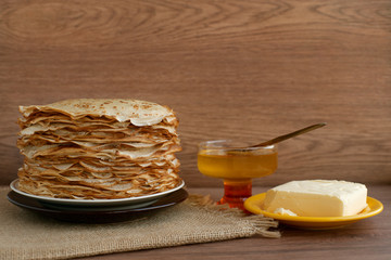 Pancakes with honey and butter. Maslenitsa. A large pile of thin pancakes with honey and butter is a sweet dessert for breakfast. Pancakes on a wooden background.