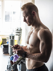 Shirtless muscular blond young man using cell phone in gym