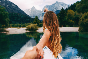 Attractive young woman holding hand of her friend and walking next to the lake