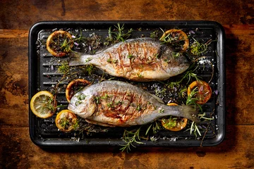 Foto op Plexiglas Grilled  fish, sea bream, dorada with the addition of spices, herbs and lemon on the grill plate located on a wooden background,  top view. Healthy eating concept © zi3000