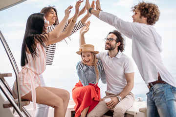 Group of friends, dressed in casual cloth, giving high five on a fashionable yacht - Happy people...