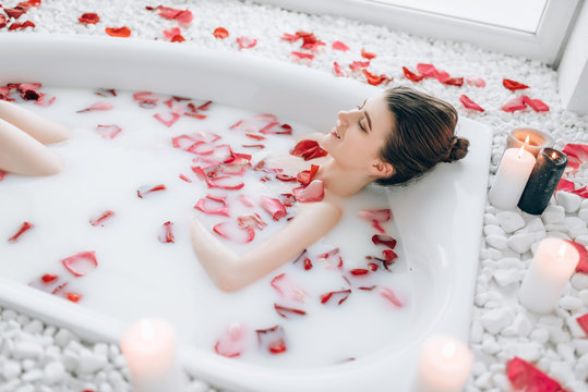 Woman sleeps in the bath with foam, rose petals