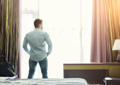 Young Man Looking Out Of The Window In Hotel Room