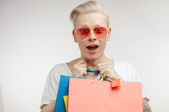 Male fashion, Man Apparel Shop, Clothing concept. Portrait of amased fashion albino male student being overjoyed with a good shopping day, keeping paper bags tightly over studio white background