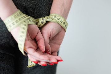 self control will power and restraint. dieting weightloss and fitness. woman hands tied with measuring tape behind her back