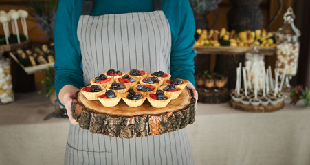 Chef holding wooden tray with berry tartlets