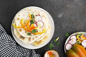 Traditional homemade flat breads for a snack with fresh seasonal vegetables, herbs and yoghurt sauce with olive oil and rose salt on the background. Top view