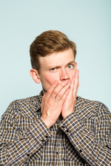 secret information. man covering mouth with hands. not telling you anything or speaking. silence and mystery. portrait of a young guy on light background. emotion and facial expression.