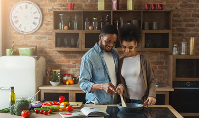 Loving black couple preparing meal together in modern kitchen