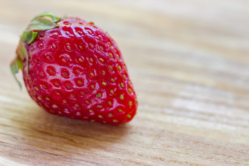 One ripe strawberry on wooden table. Close-up photo. Summer fruits
