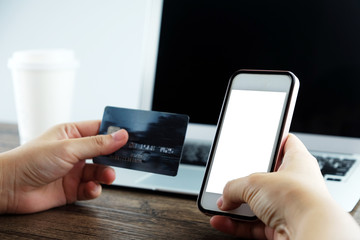 Hands of woman holding a credit card and paying by smartphone for online shopping.