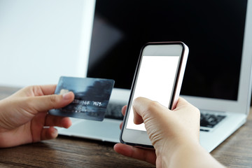 Hands of woman holding a credit card and paying by smartphone for online shopping.