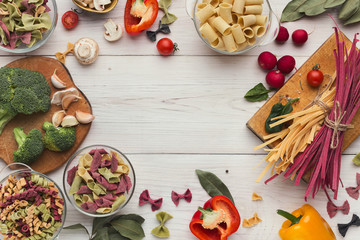 Mixed italian pasta and vegetables on white wood, top view