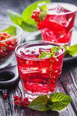 Red currant cocktail with ice and fresh mint on a black wooden table