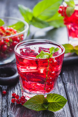 Red currant cocktail with ice and fresh mint on a black wooden table