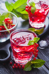 Red currant cocktail with ice and fresh mint on a black wooden table