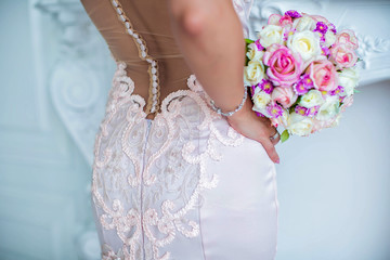 Bride stands with her back, holds wedding bouquet in her hands, near waist, closeup