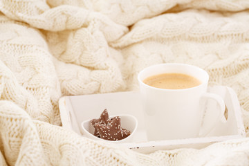 Hot beverage mug with chocolate cookies in a white wool blanket. Hot drink, cozy home and cold season concept