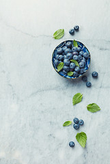 Fresh ripe blueberries with mint leaves in a bowl on gray marble background. Flat lay. Copy space.