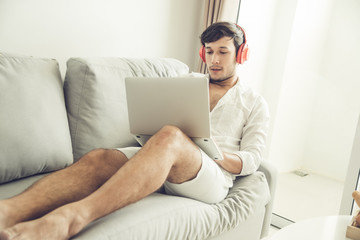 Happy man relaxing on the sofa listening to music with laptop at home