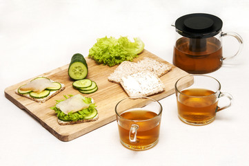 Healthy breakfast with whole grain bread, fresh vegetables, white fish and green tea on white fabric background