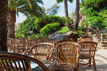 Obraz premium Old wicker chairs on a sandy terrace with sea views surrounded by palm trees. Tropical landscape.