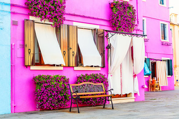 Naklejka premium Różowy dom z różowymi kwiatami i roślinami. Ładna ławka pod oknami. Kolorowy dom na wyspie Burano w pobliżu Wenecji, Włochy