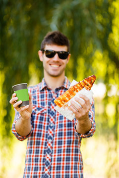Man eating pizza. Cheerful young guy is eating pizza drinking coffee on the park