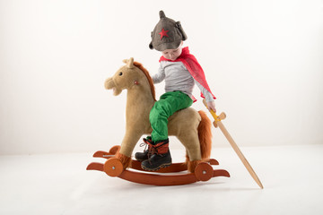 Funny child in old military cap with red star, on toy horse-rocking horse with wooden sword. Boy...