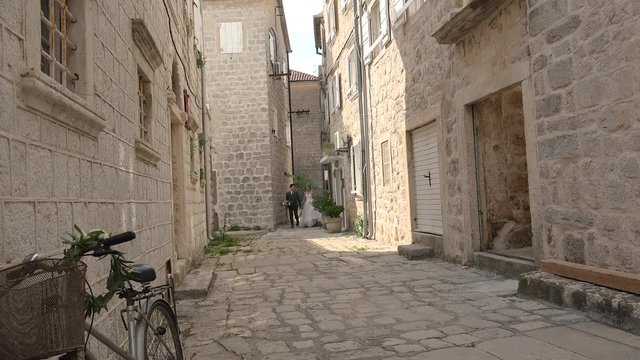 Newlyweds are walking along a narrow cobbled street of the medieval town. Perast, Montenegro.
