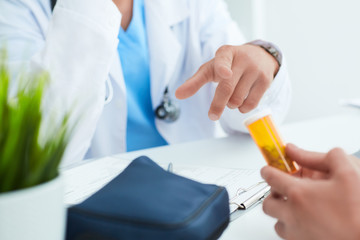 Bottle of pills in the hands of the patient close-up. Male doctor gesticulating explains how to take the drug in the background.