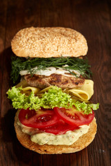 Close-up of traditional american burger with lettuce, cheese, onion and tomato on wooden background, vertical