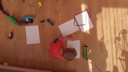 the little boy draws on paper, on the floor.