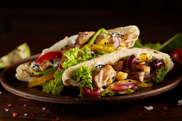 Exotic stuffed pita with fresh vegetables and beans in clay plate over wooden background, selective focus.