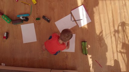 the little boy draws on paper, on the floor.