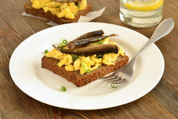 Sandwich with scrambled eggs and sprats on rye bread
