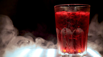 A barman stirs a spoon with a red cocktail with ice, fresh, cold, alcohol, black background.