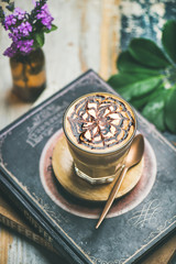 Latte coffee with chocolate sauce pattern in tall glass over rustic table with books background, selective focus