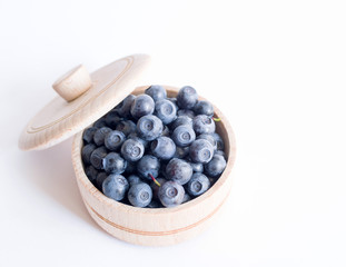 Fresh forest blueberries in a wooden cup on a white background closeup, top view.