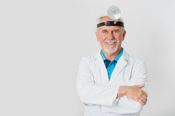 smiling ENT doctor, elderly man standing at light background