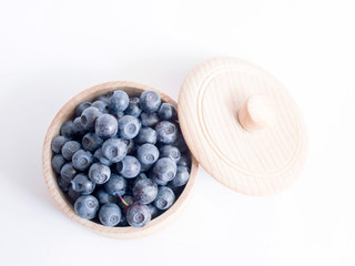 Fresh forest blueberries in a wooden cup on a white background closeup, top view.