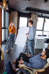 Young caucasian man coach holding flip chart, explaining studying materiel in stylish meeting room...