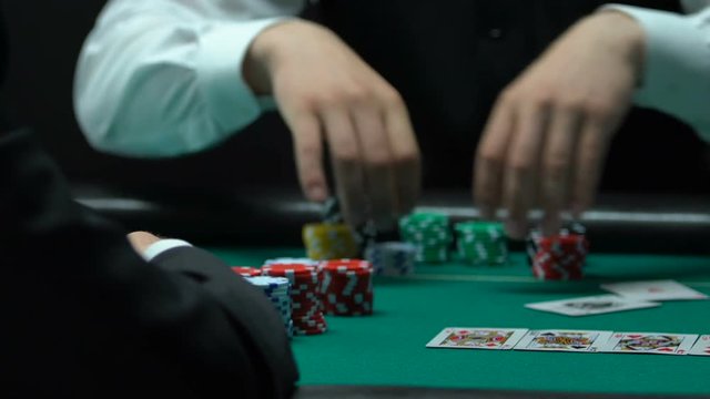 Player exposes two aces in poker, croupier moves chips to winner, closeup