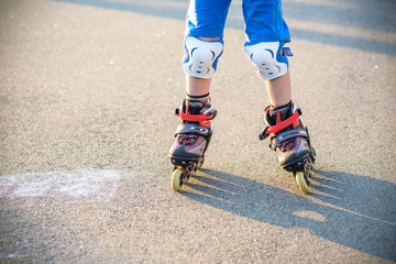 Fototapeta na wymiar Little boy learning to roller skate in summer park. Children wearing protection pads for safe roller skating ride. Active outdoor sport for kids. Close up view of skates
