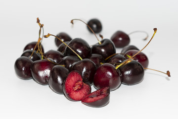 berries of red ripe cherries and one cut in half, on white background, close-up